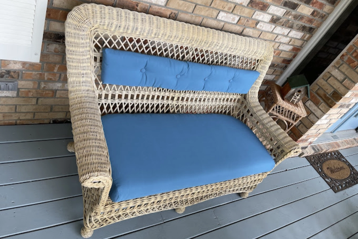 A wicker couch with blue cushions on the front porch.